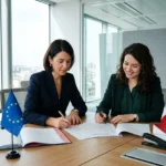 Deux femmes en réunion signent des documents, entourées de drapeaux EU, France et Roumanie, dans une salle de conférence lumineuse. Détachement roumanie.