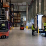 Agence intérim logistique: opérateurs en zone de stockage manipulant palettes et manutentionnaires près d’un quai de chargement dans un entrepôt.